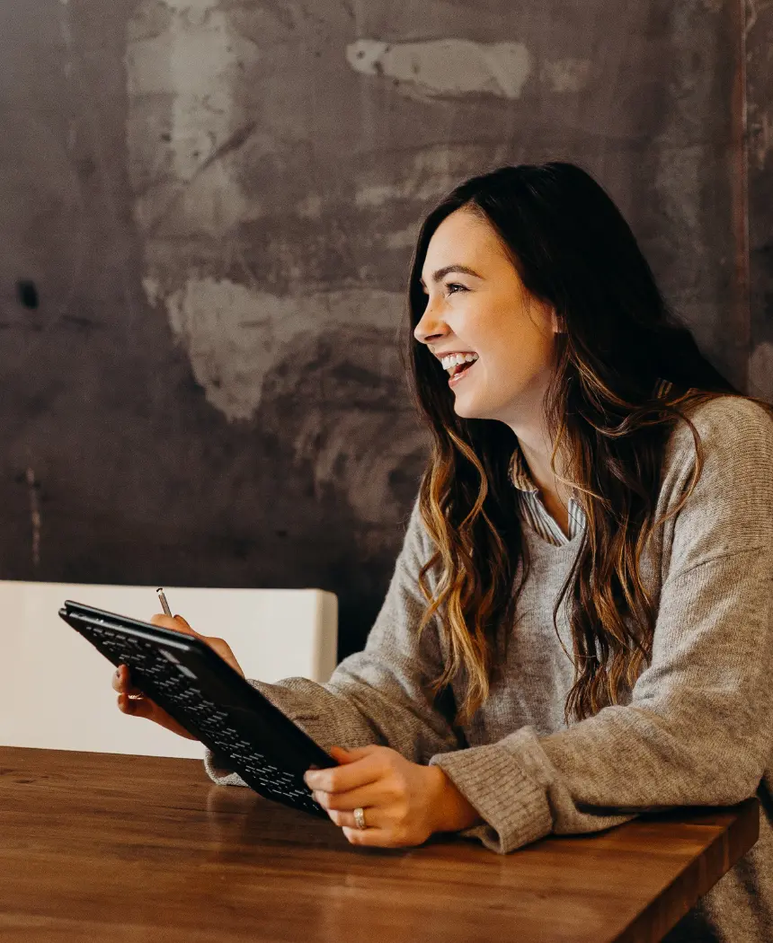 A woman with a tablet in her hands at a wooden table.