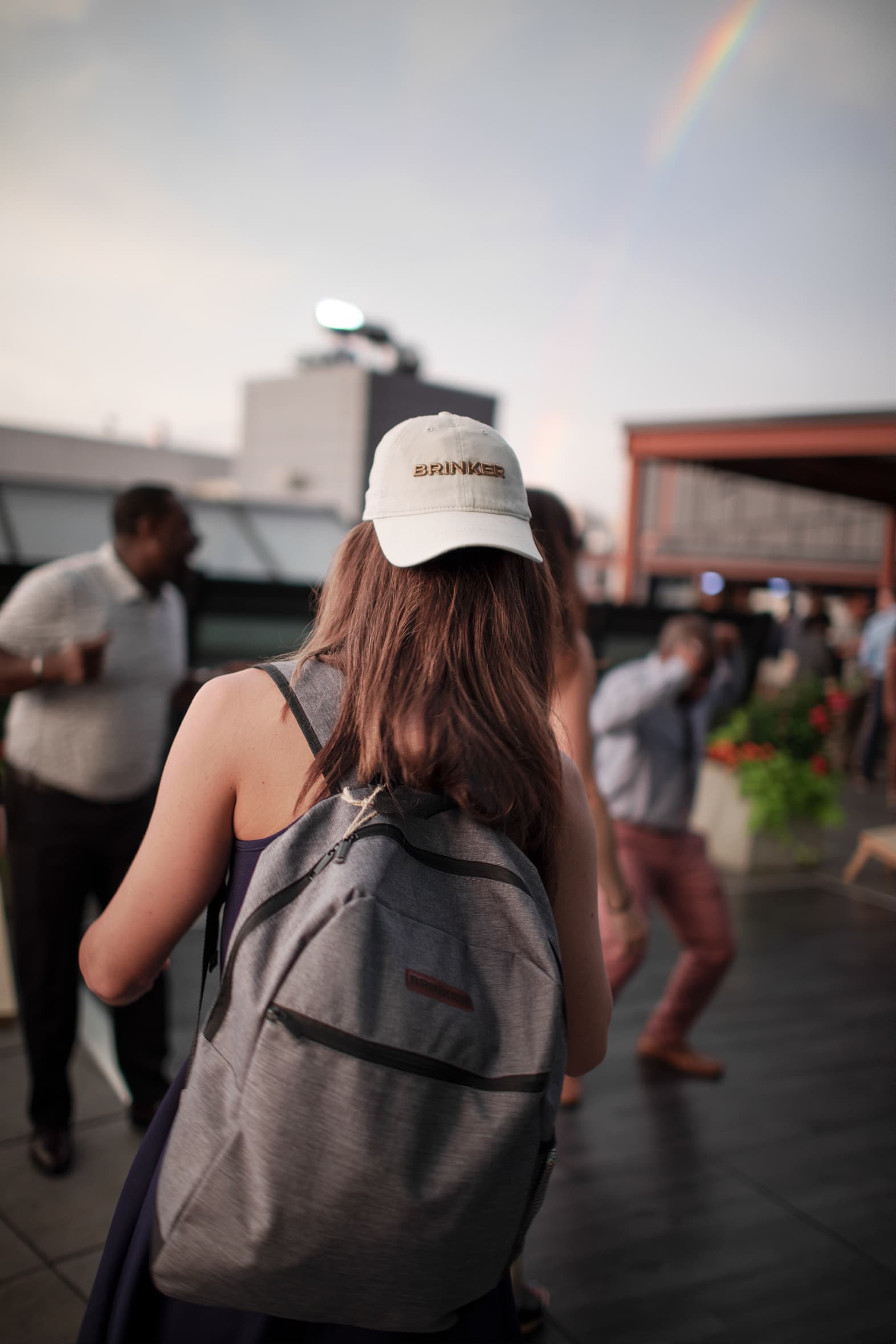 A lady with a Brinker branded baseball cap and a backpack watching the stage at the Brinker brand launch.