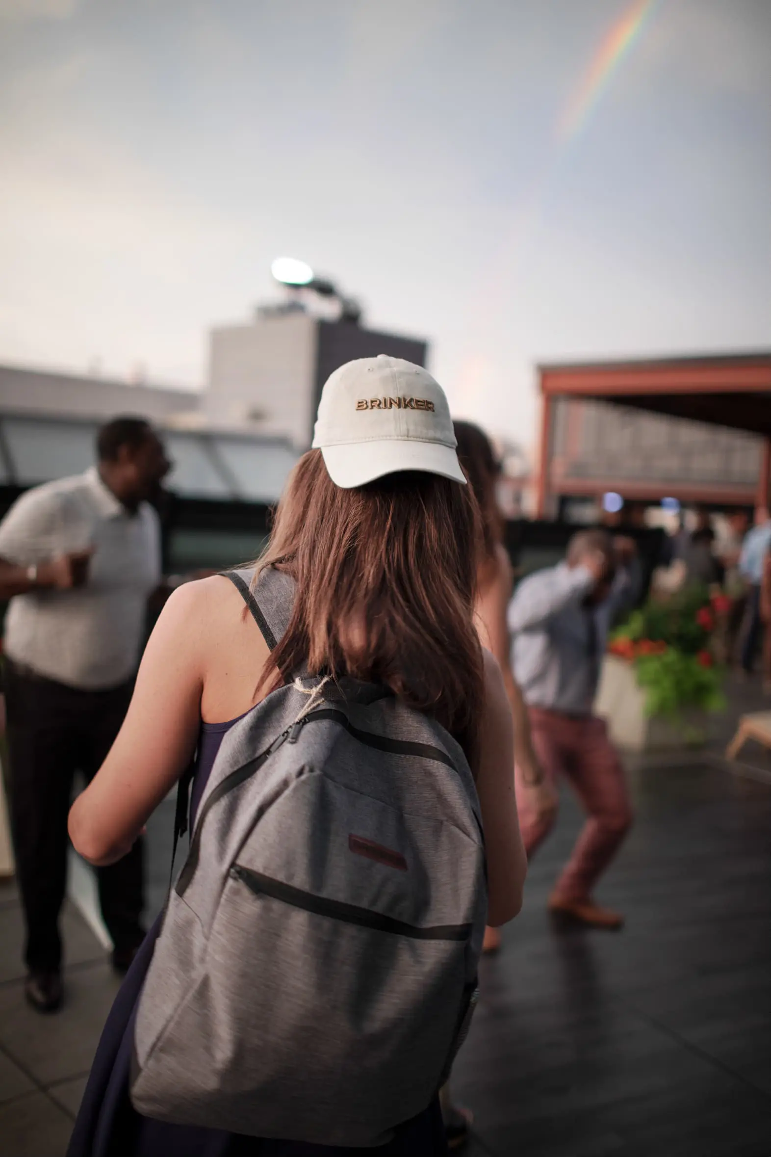 A lady with a Brinker branded baseball cap and a backpack watching the stage at the Brinker brand launch.