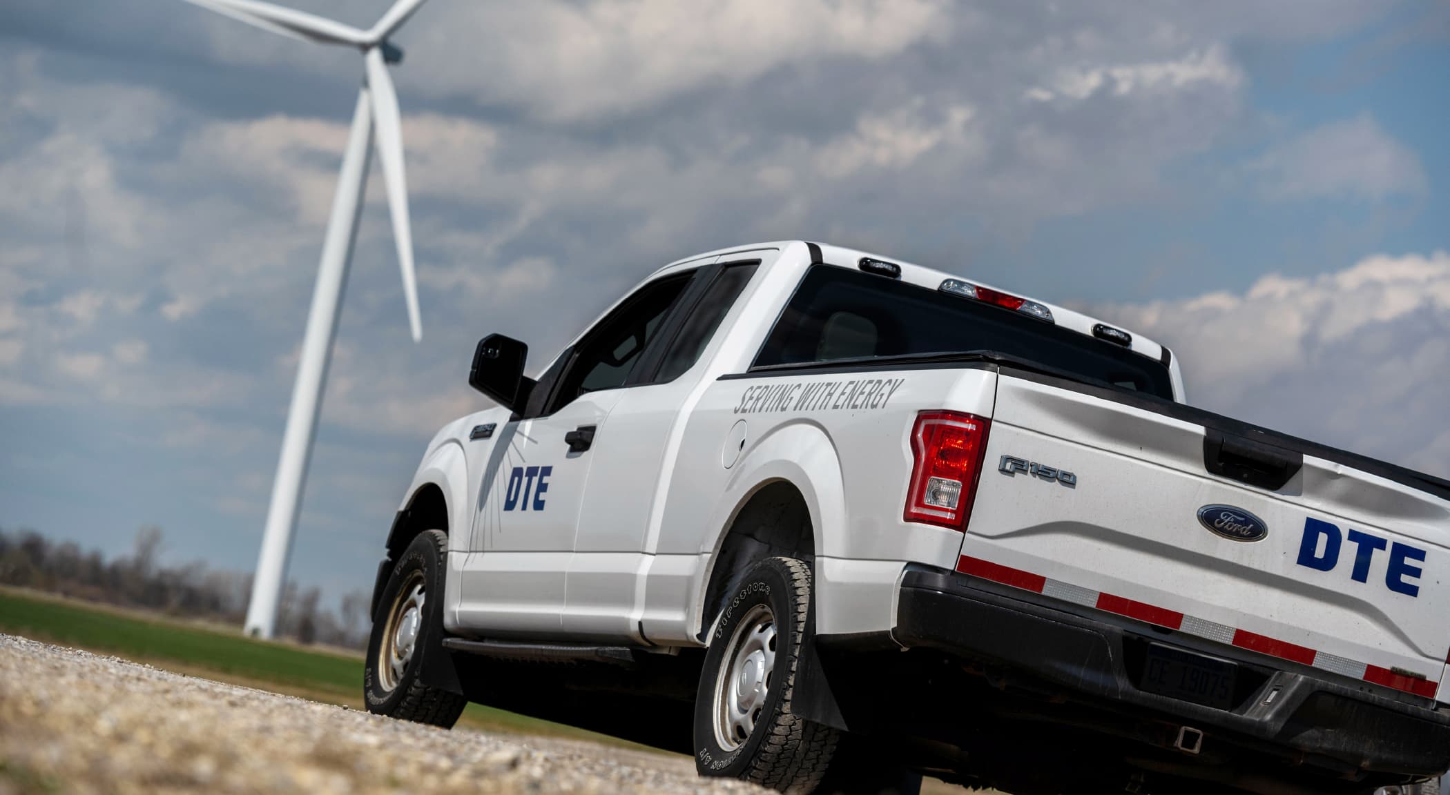 DTE logo'd pickup truck at the bottom of a wind generator.