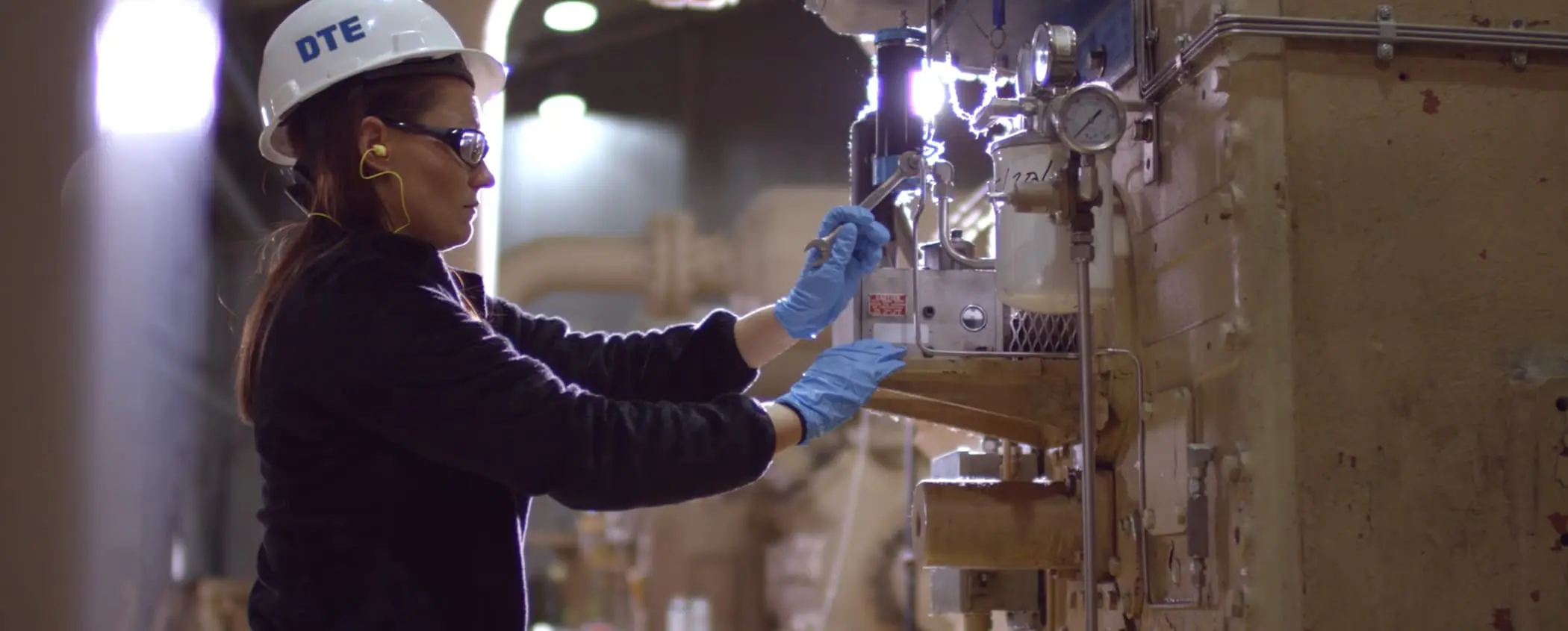 DTE crew wrenching a nut on a pipe in a industrial mechanical room.
