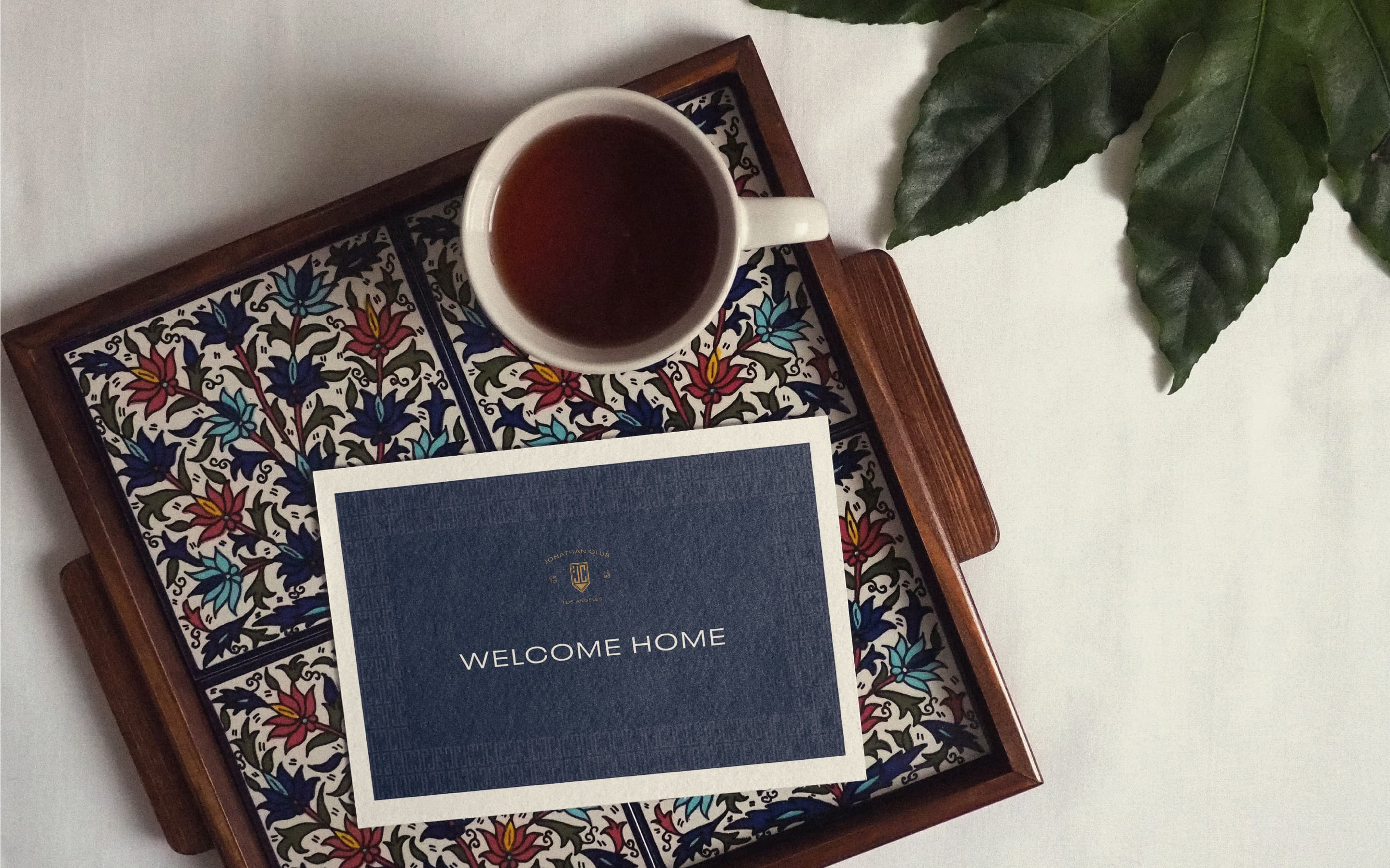 Welcome card and a mug of coffee on a colorful flower tiled tray.