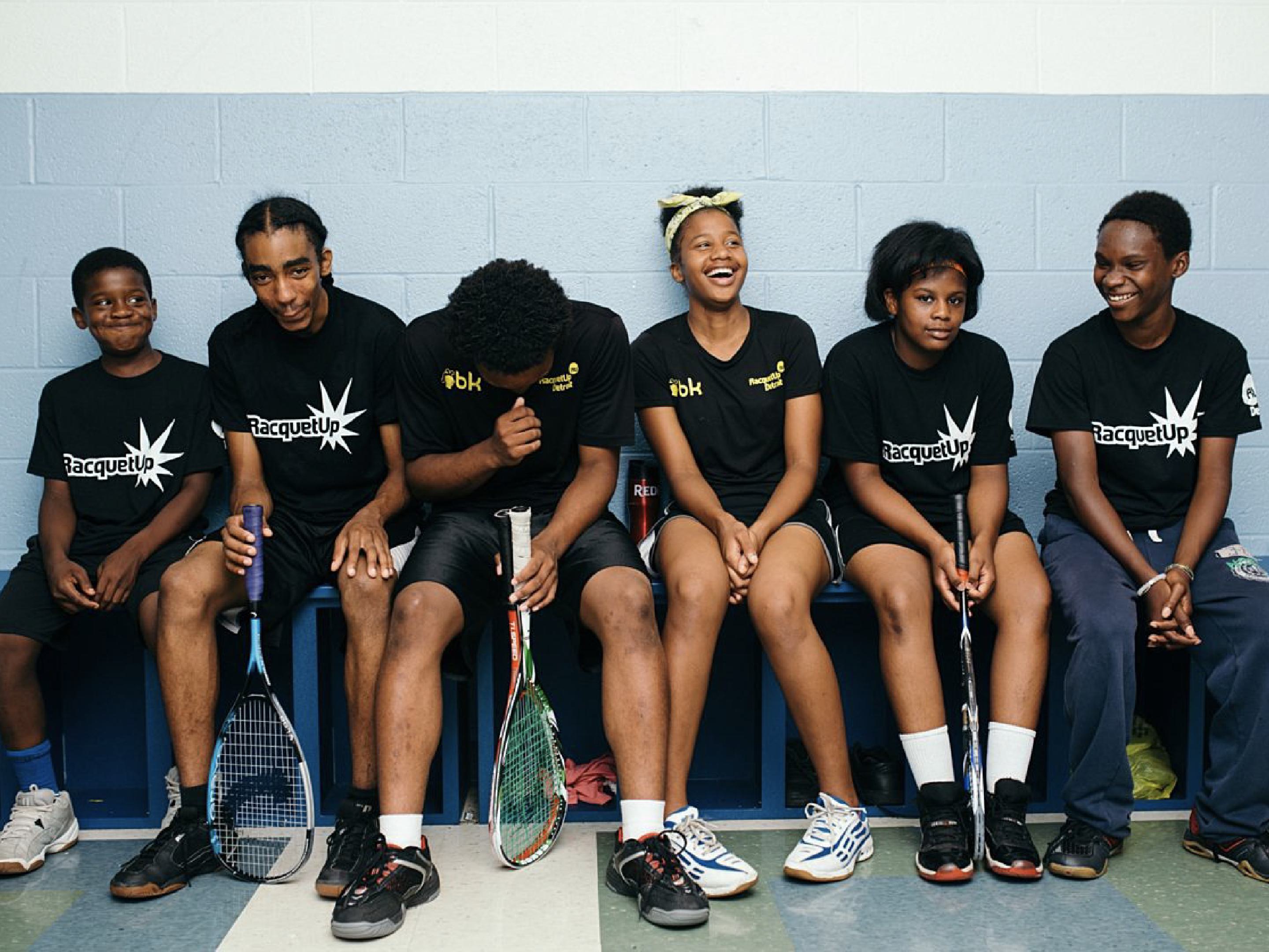 Six young kids wearing black RUD branded t-shirts with racquets having fun with each other.